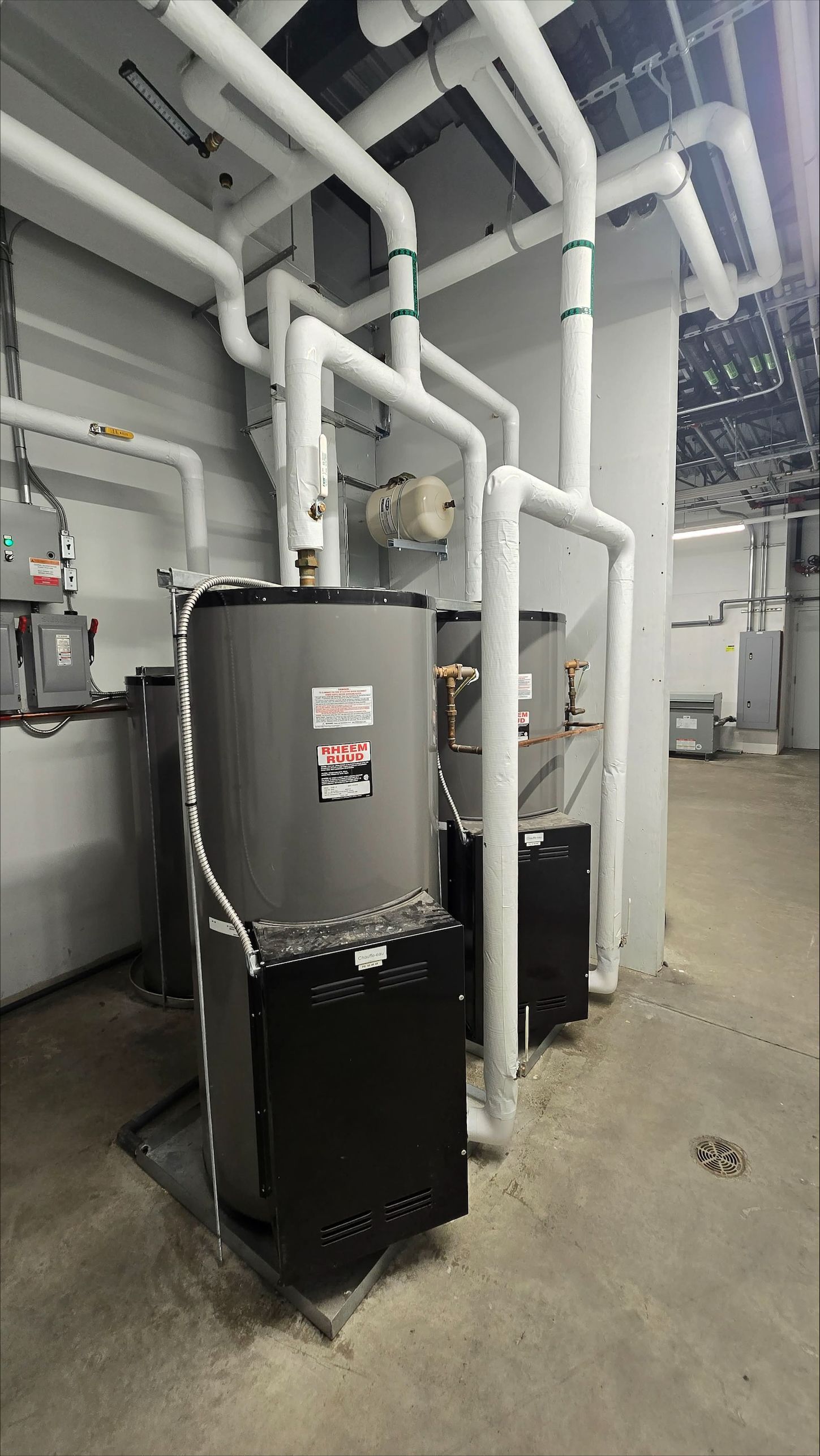 Deux chauffe-eau industriels avec un important réseau de tuyauterie blanche dans un local technique.