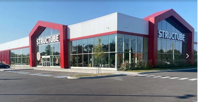 Un bâtiment moderne de plain-pied abritant un magasin de meubles Structube, avec de grandes fenêtres et des accents architecturaux rouges distinctifs.