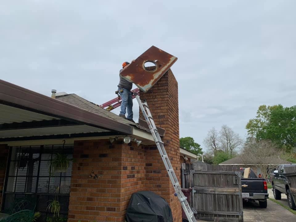 Man on a ladder removing a rusty metal panel from a brick chimney on a house. Overcast day.