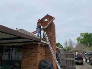 Person on a ladder removing rusty metal sheet from a brick chimney on a house roof.