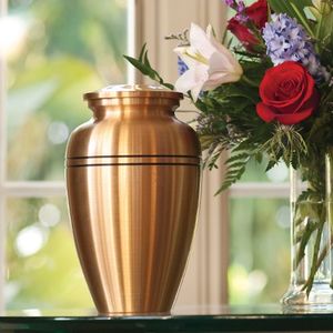 Copper funeral urn beside a red, white, and blue flower arrangement in a sunlit room