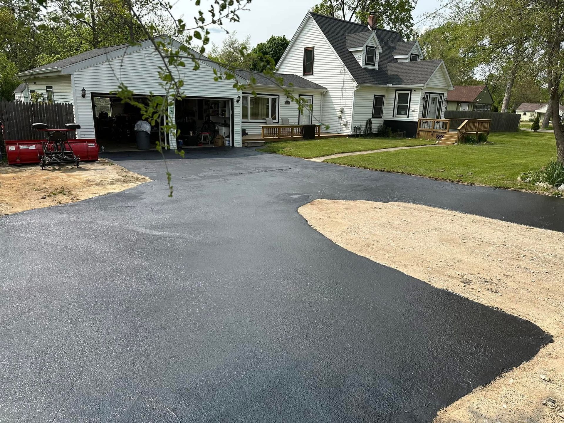 Fresh black asphalt driveway curving past a white house and garage, with a gravel patch in front