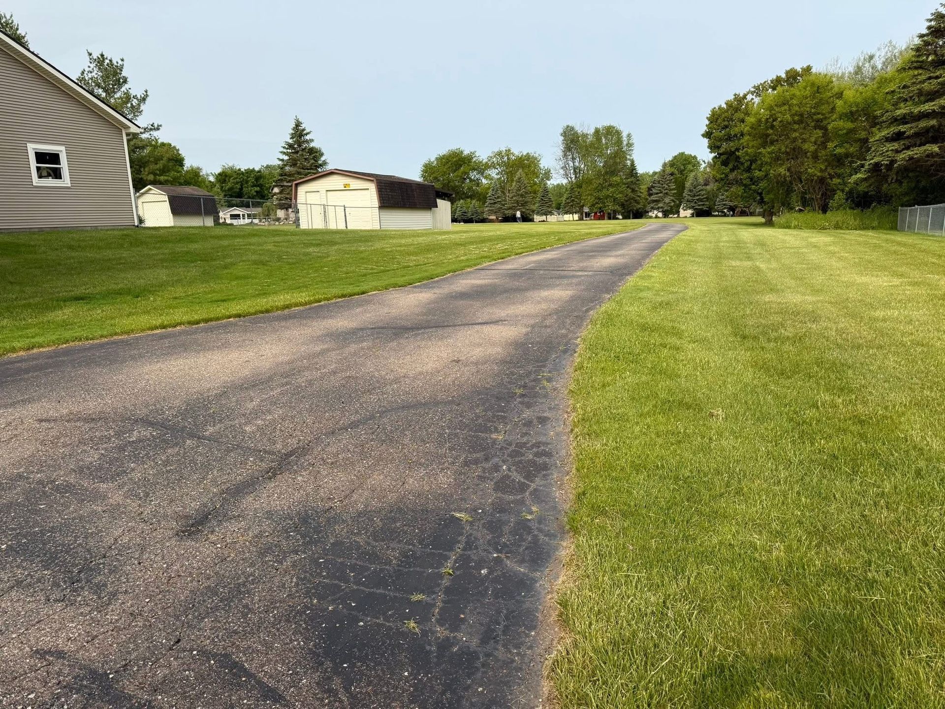 Paved driveway through a grassy yard beside houses on a sunny day