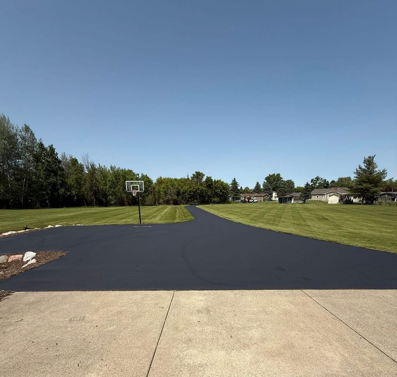 Freshly paved driveway in front of a white garage and house, with a truck and trees in the background