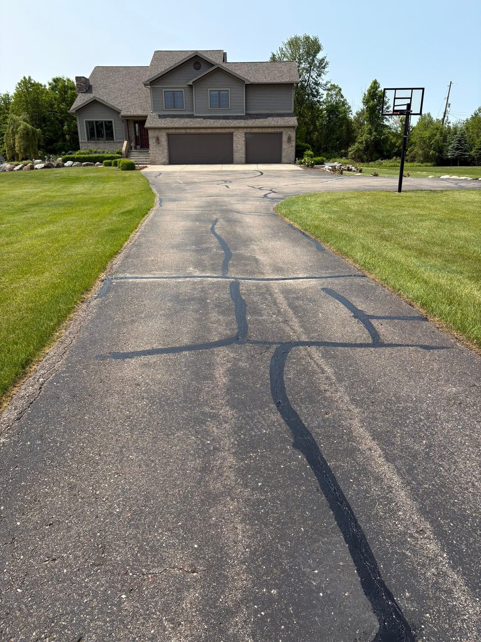 Cracked driveway leading to a two-story suburban house with a garage and green lawn.