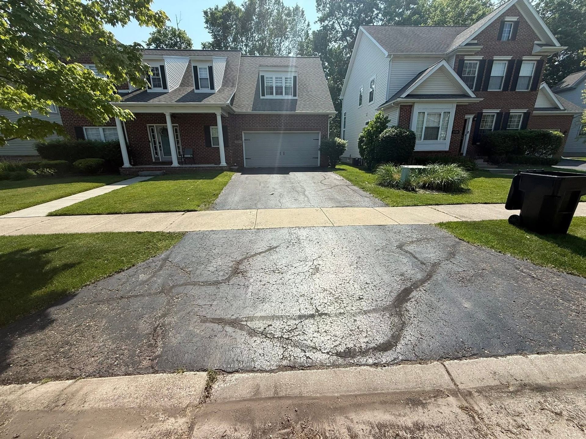 Suburban driveway and two-story homes with a cracked asphalt street in the foreground