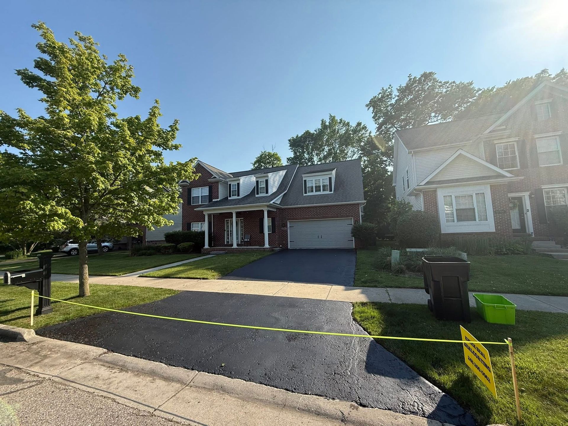 Suburban house with driveway, green lawn, and trees on a sunny day