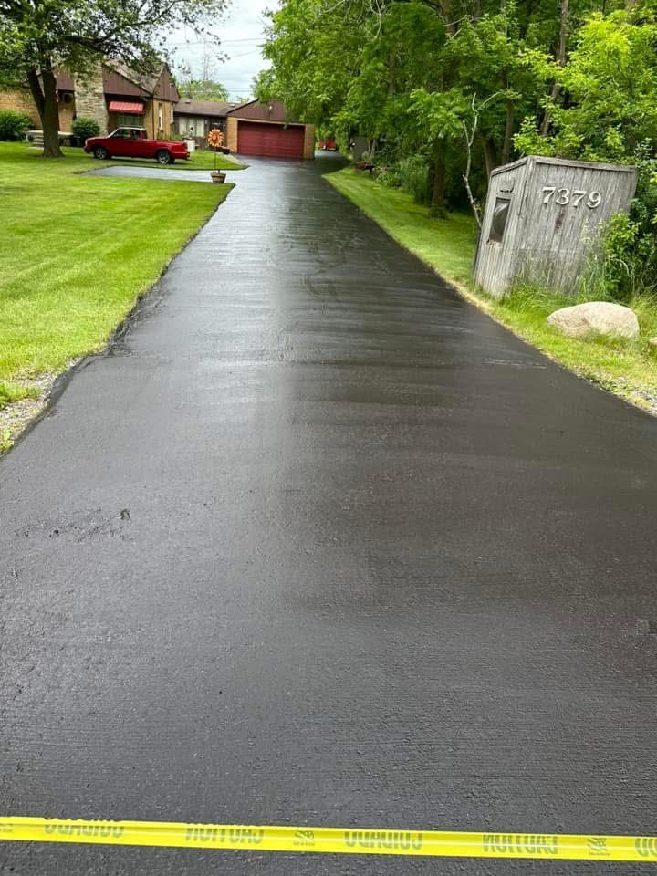 Wet black driveway leading to a red house and garage, with yellow caution tape in the foreground.