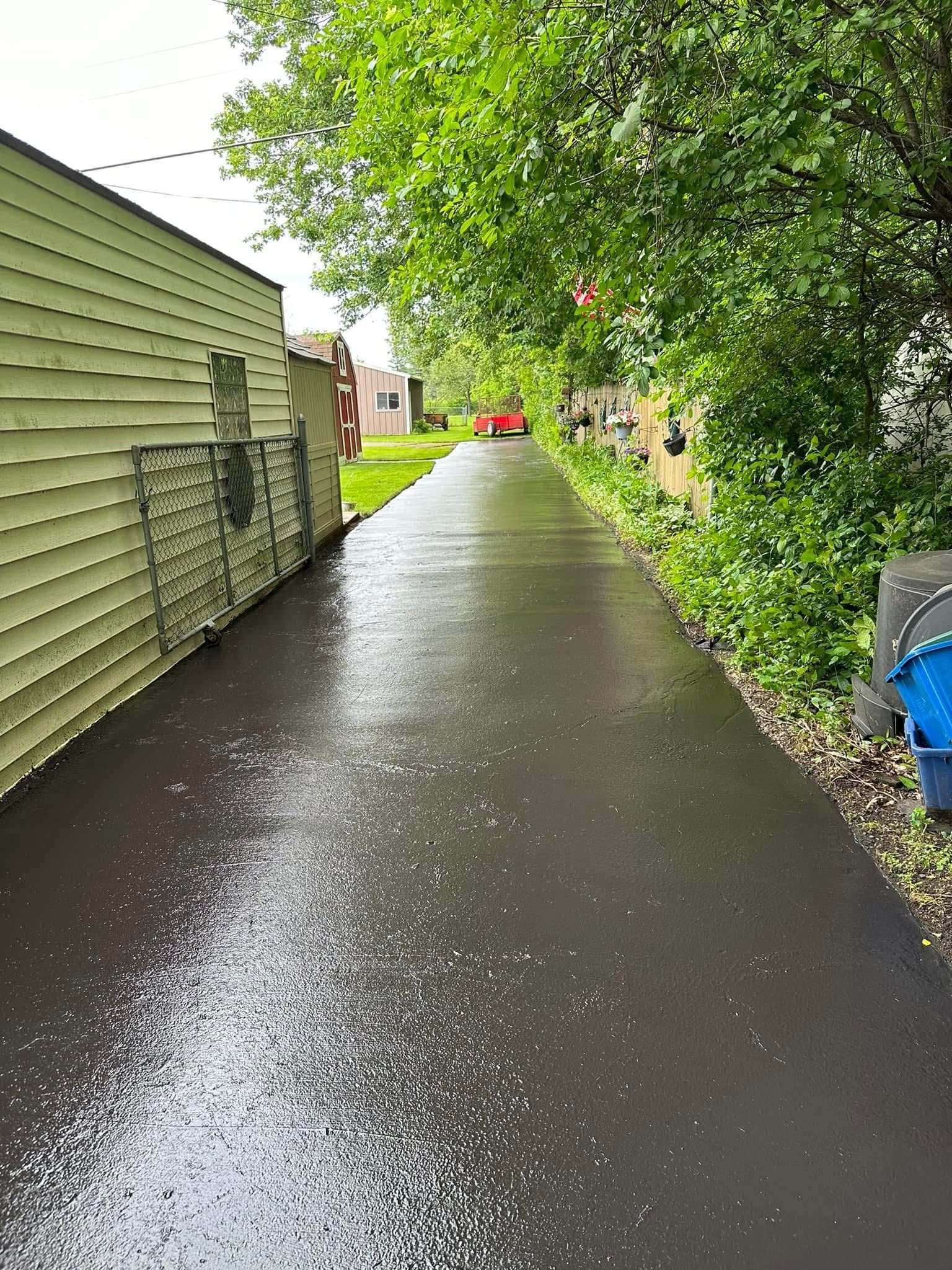 Rain-slicked driveway beside a house, lined with trees and greenery on a cloudy day