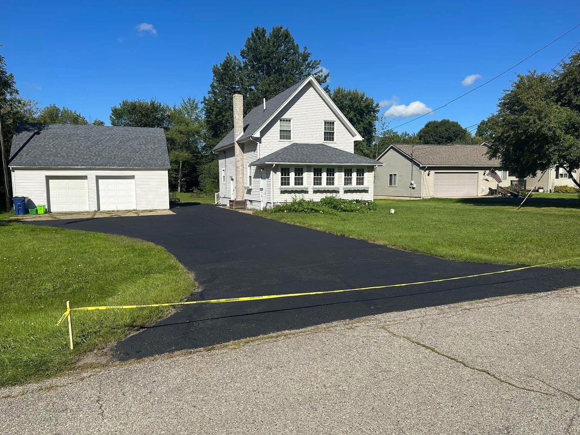 Suburban house with a fresh black driveway beside a detached garage on a sunny day