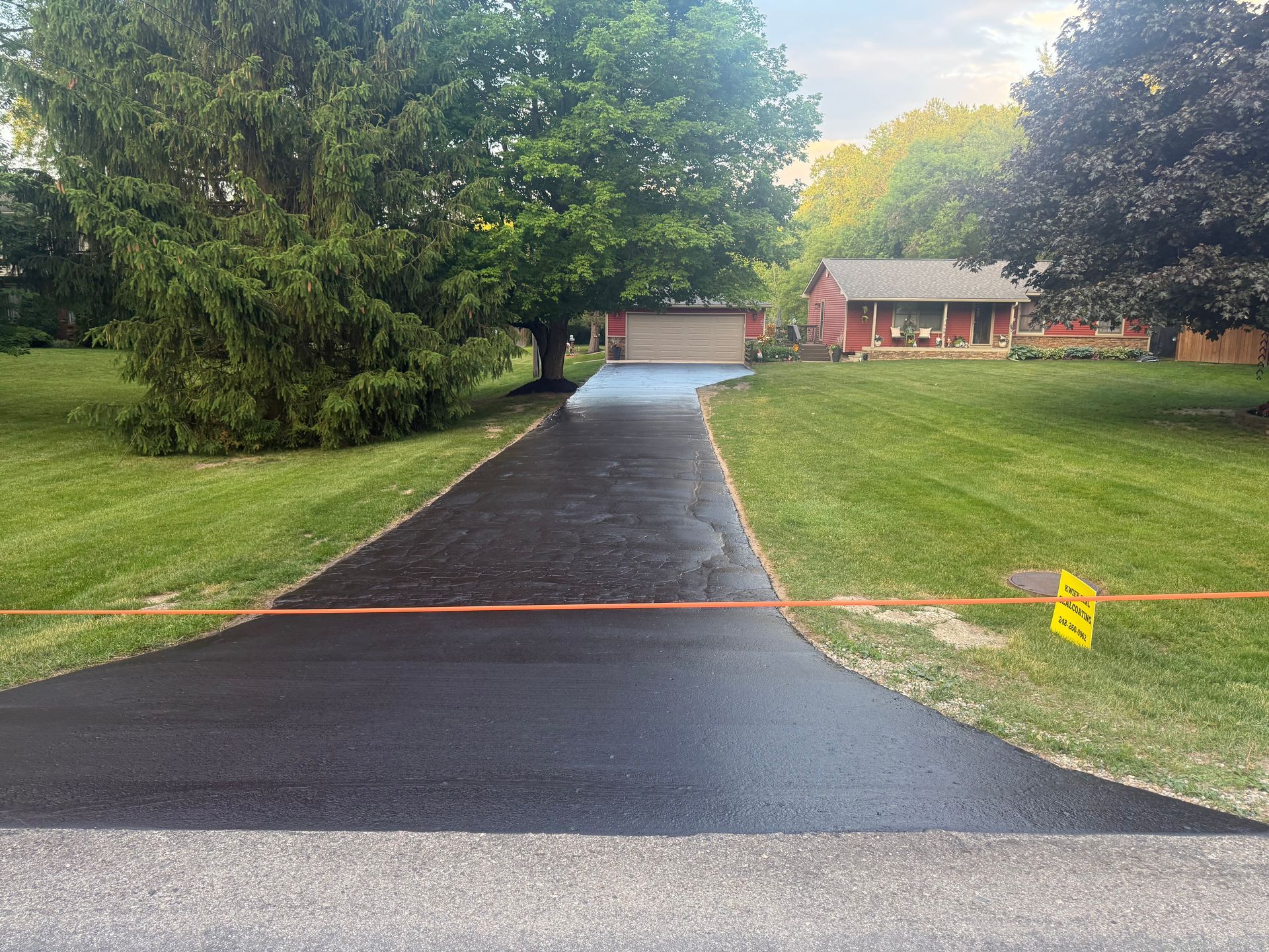 Freshly paved driveway leading to a house and garage, with trees and lawn on both sides.