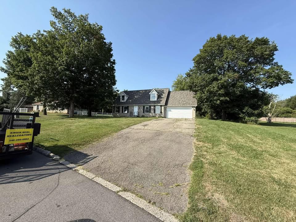Suburban house with a gravel driveway, white garage, and two large trees under a clear blue sky