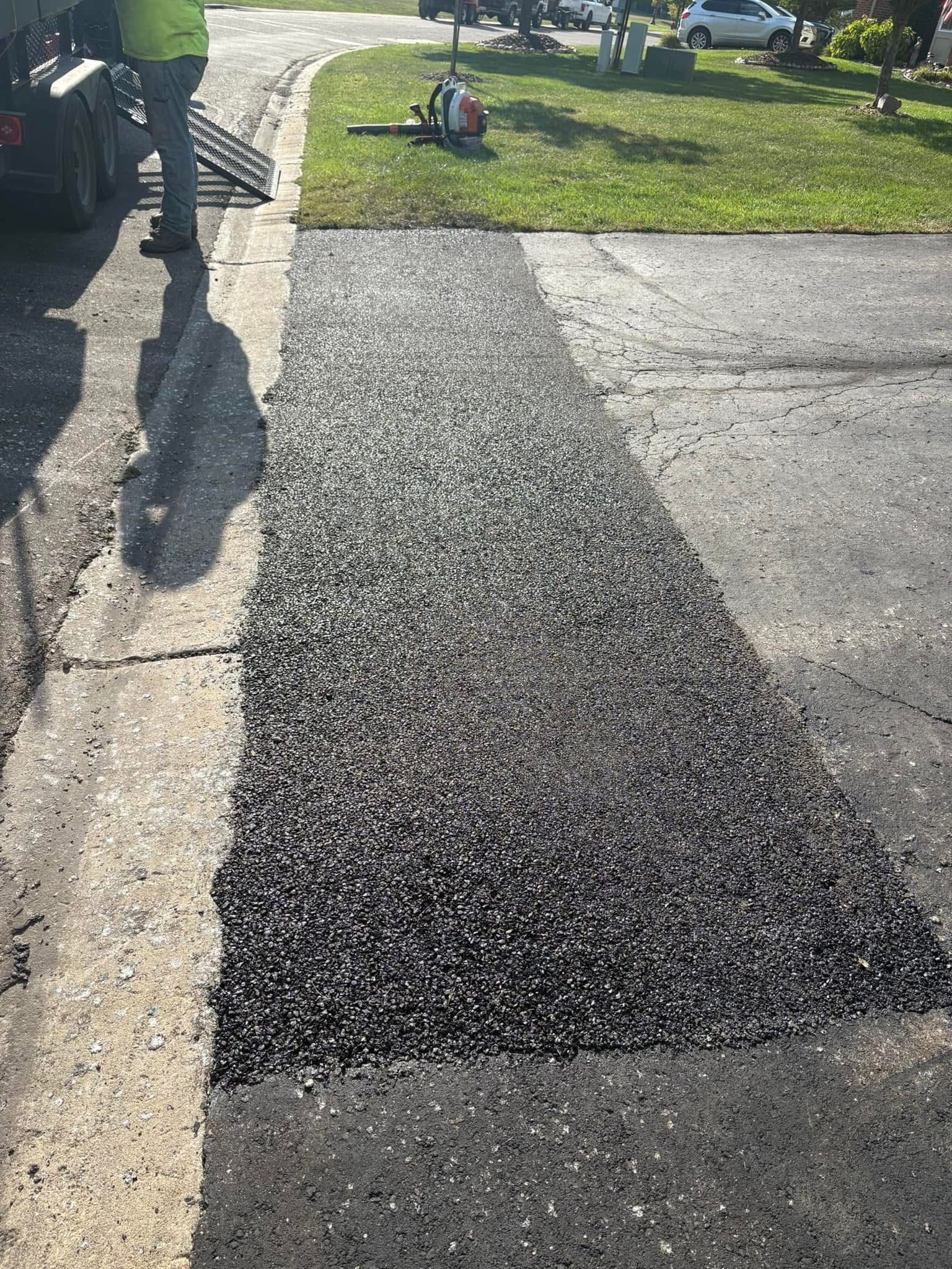 Freshly paved black driveway strip beside an existing concrete driveway and lawn