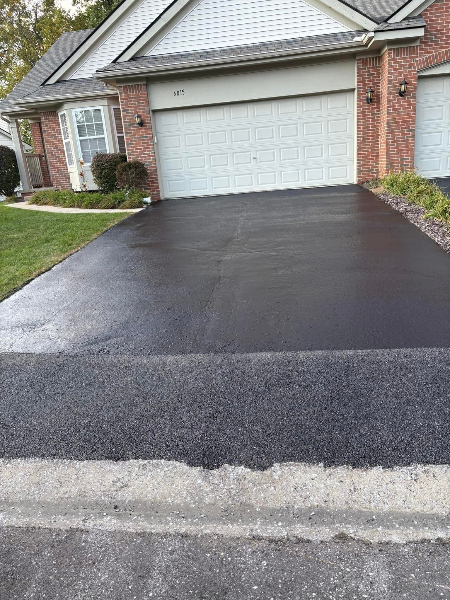 Freshly paved black driveway leading to a white garage at a brick house