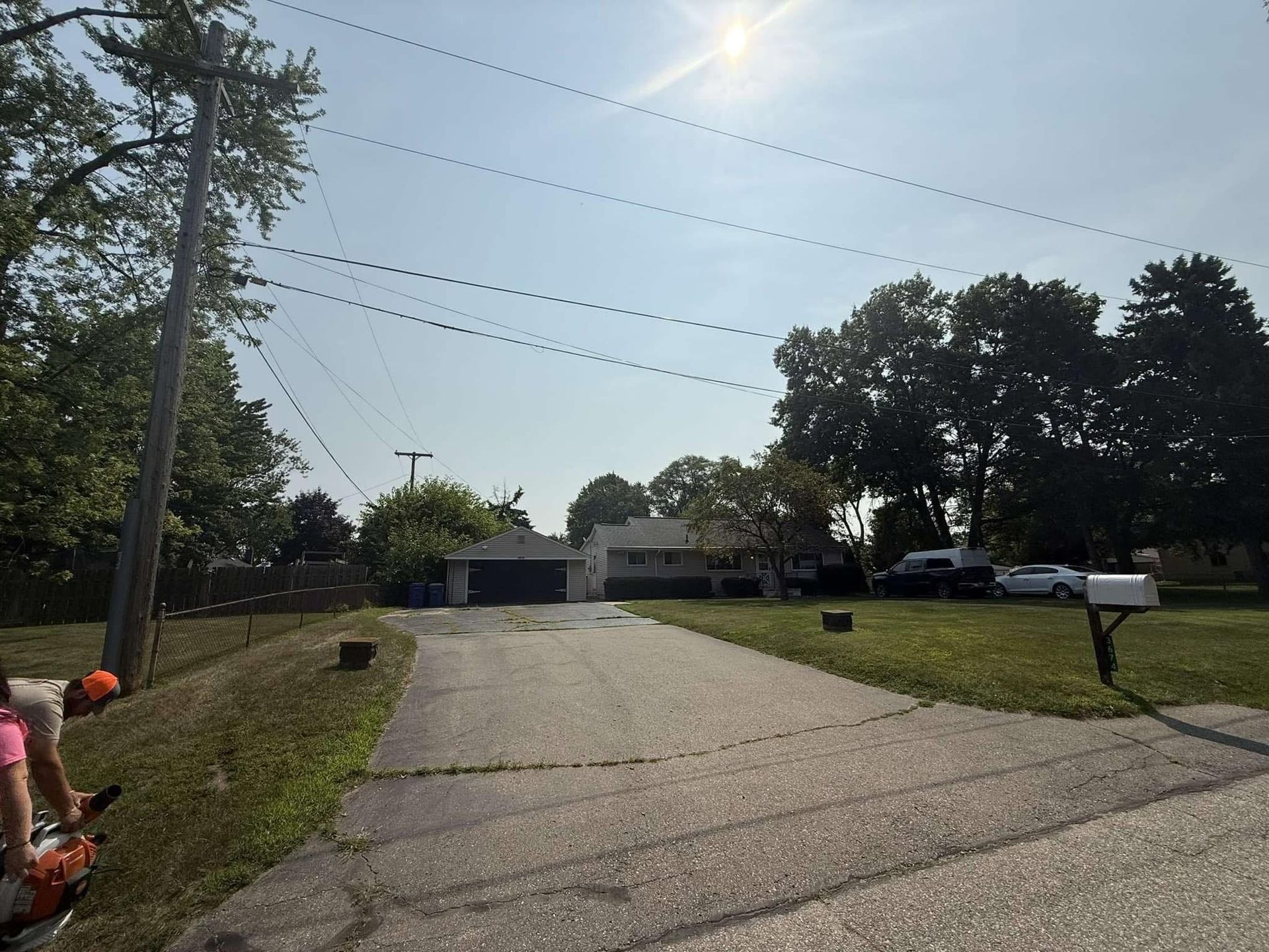 Driveway leading to a suburban house, with utility poles, parked cars, and a bright sunny sky.