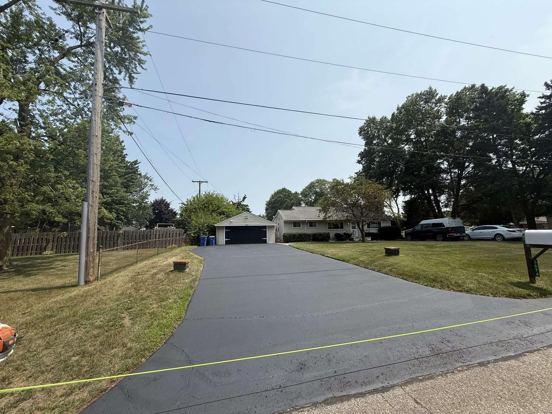 Freshly paved driveway leading to a house and garage, with utility poles and trees on a sunny day