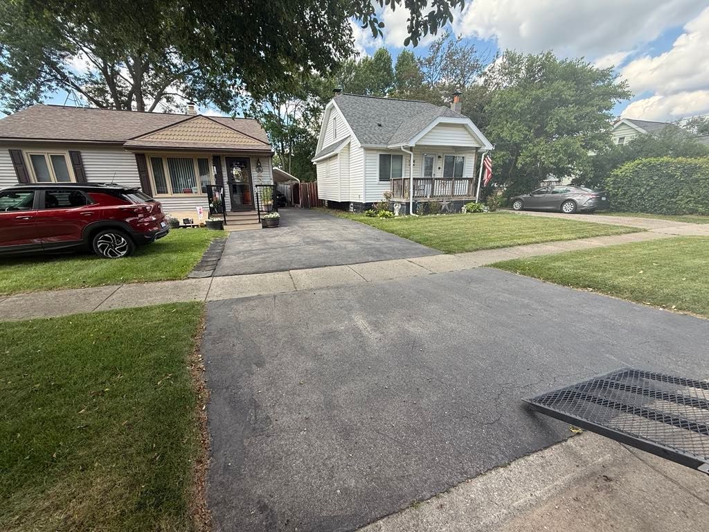Suburban driveway between two houses, with a red SUV parked on the left and a storm drain in the foreground