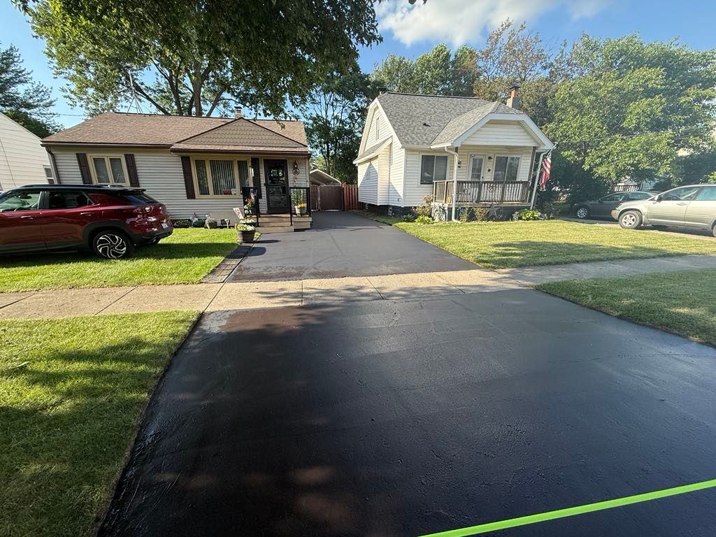 Suburban street with two small houses, parked cars, and a long driveway under sunny trees