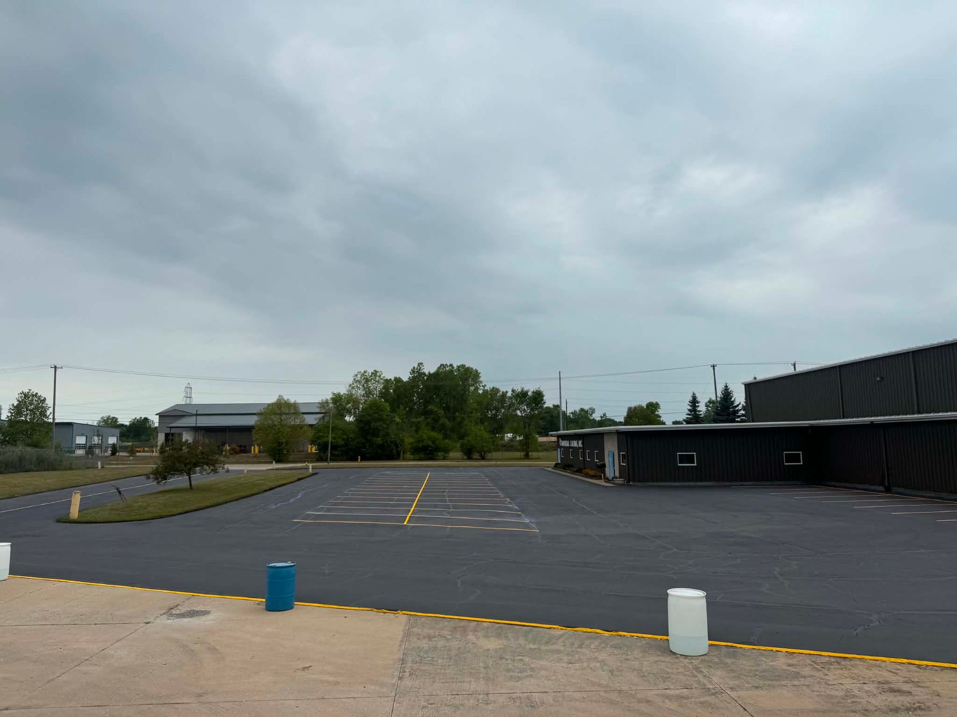 Empty asphalt parking lot beside low buildings under cloudy sky