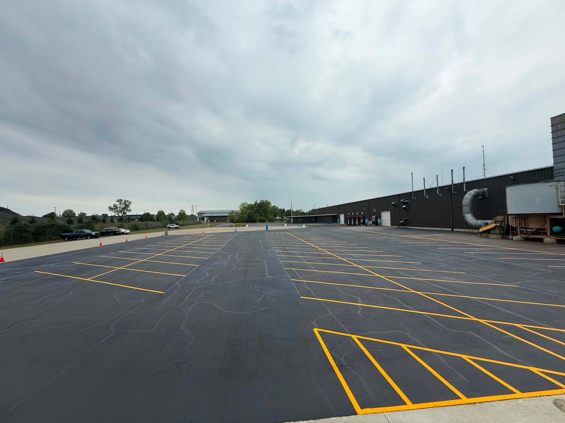 Empty airport tarmac with yellow markings beside a terminal and parked trucks under cloudy skies