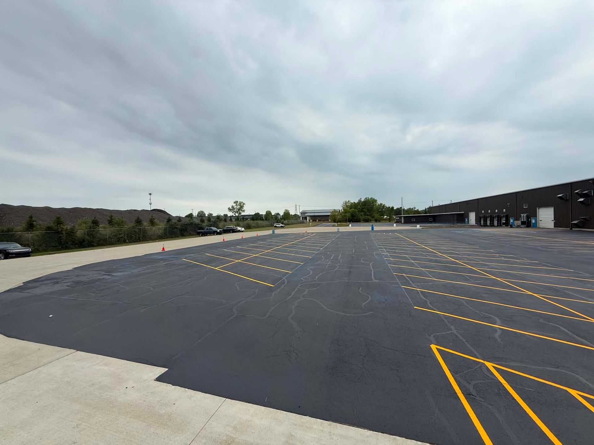 Empty asphalt parking lot with yellow diagonal stripes beside a low building under cloudy skies
