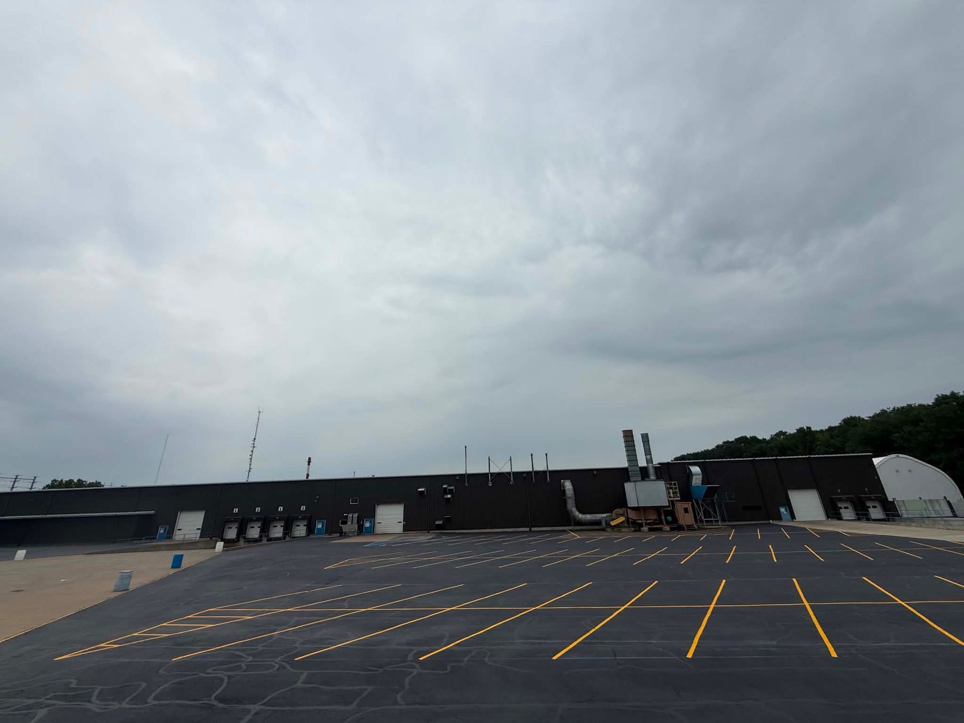Empty parking lot with yellow lines beside a long black building under a cloudy sky