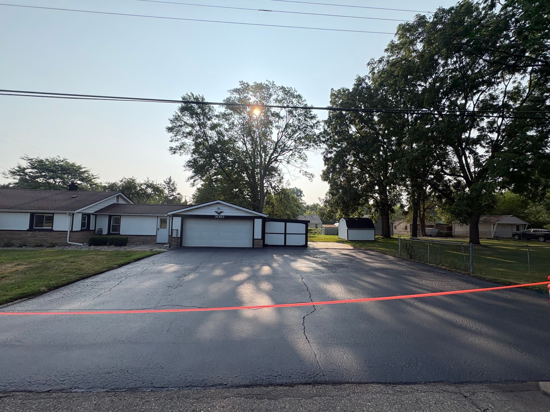 Driveway leading to three garage doors at dusk, with trees and a low house in the background.