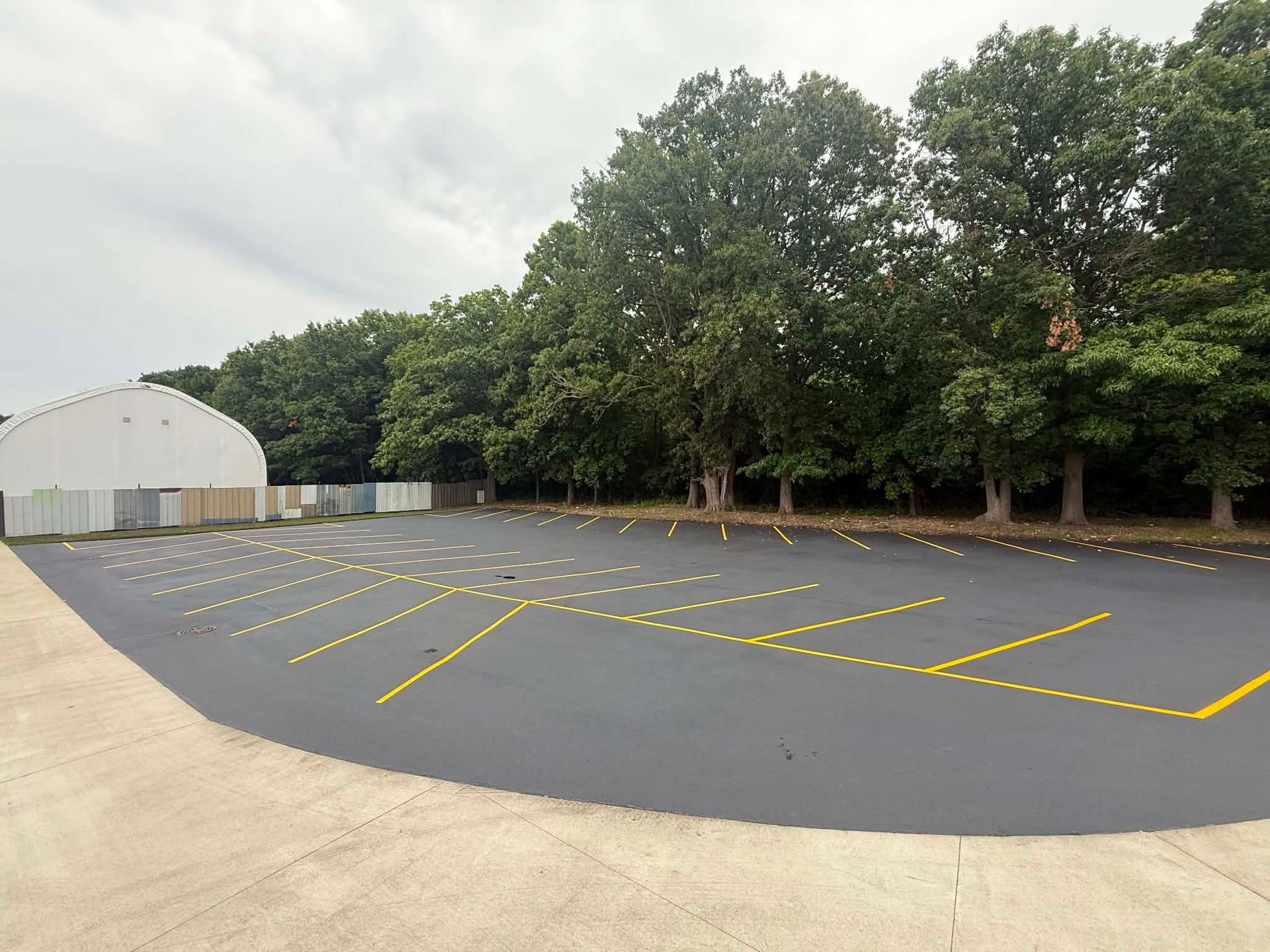 Empty asphalt lot with yellow parking lines beside trees and a white building