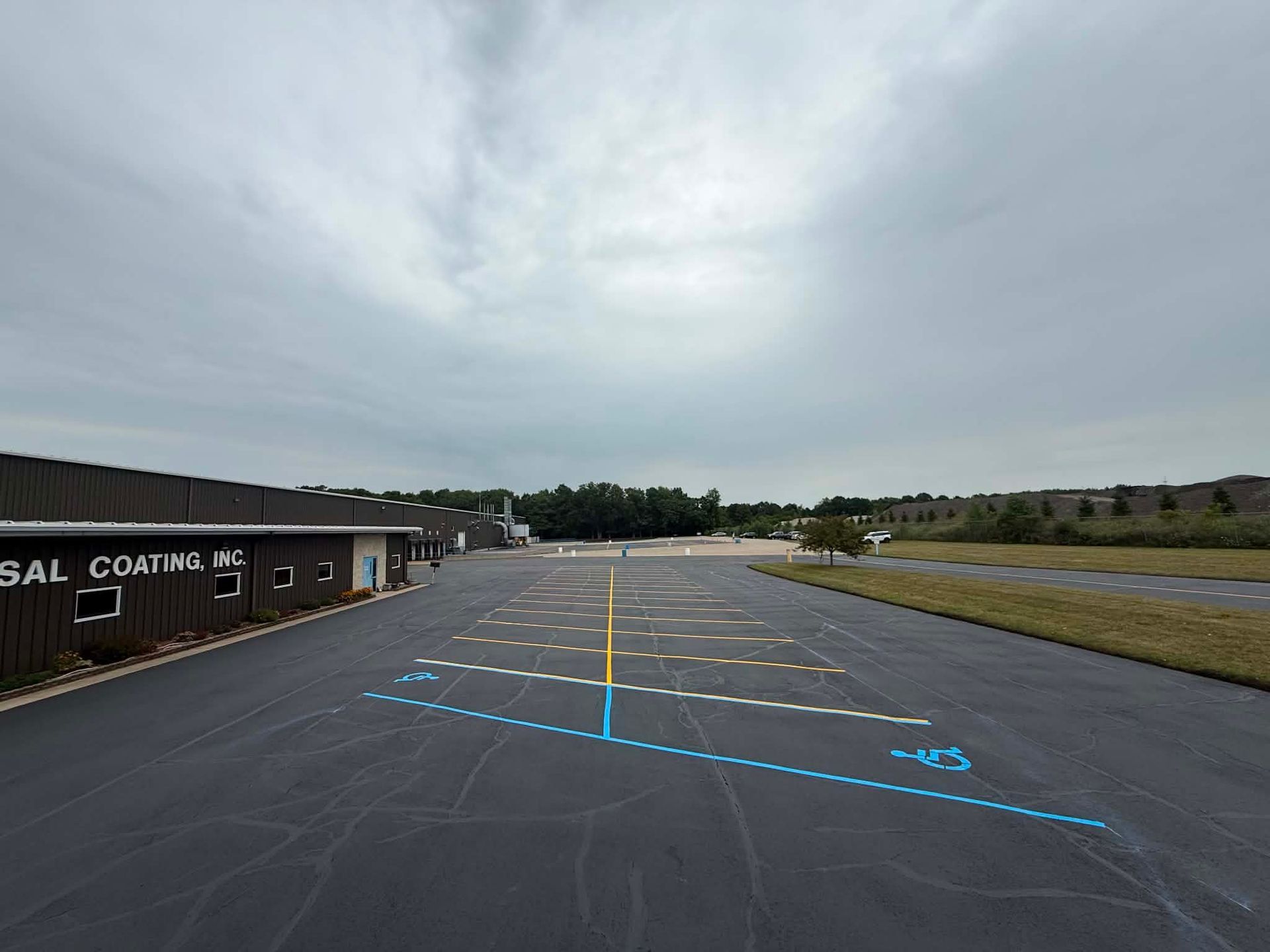 Empty airport taxiway with blue and white markings under a cloudy sky, next to a building and grassy field