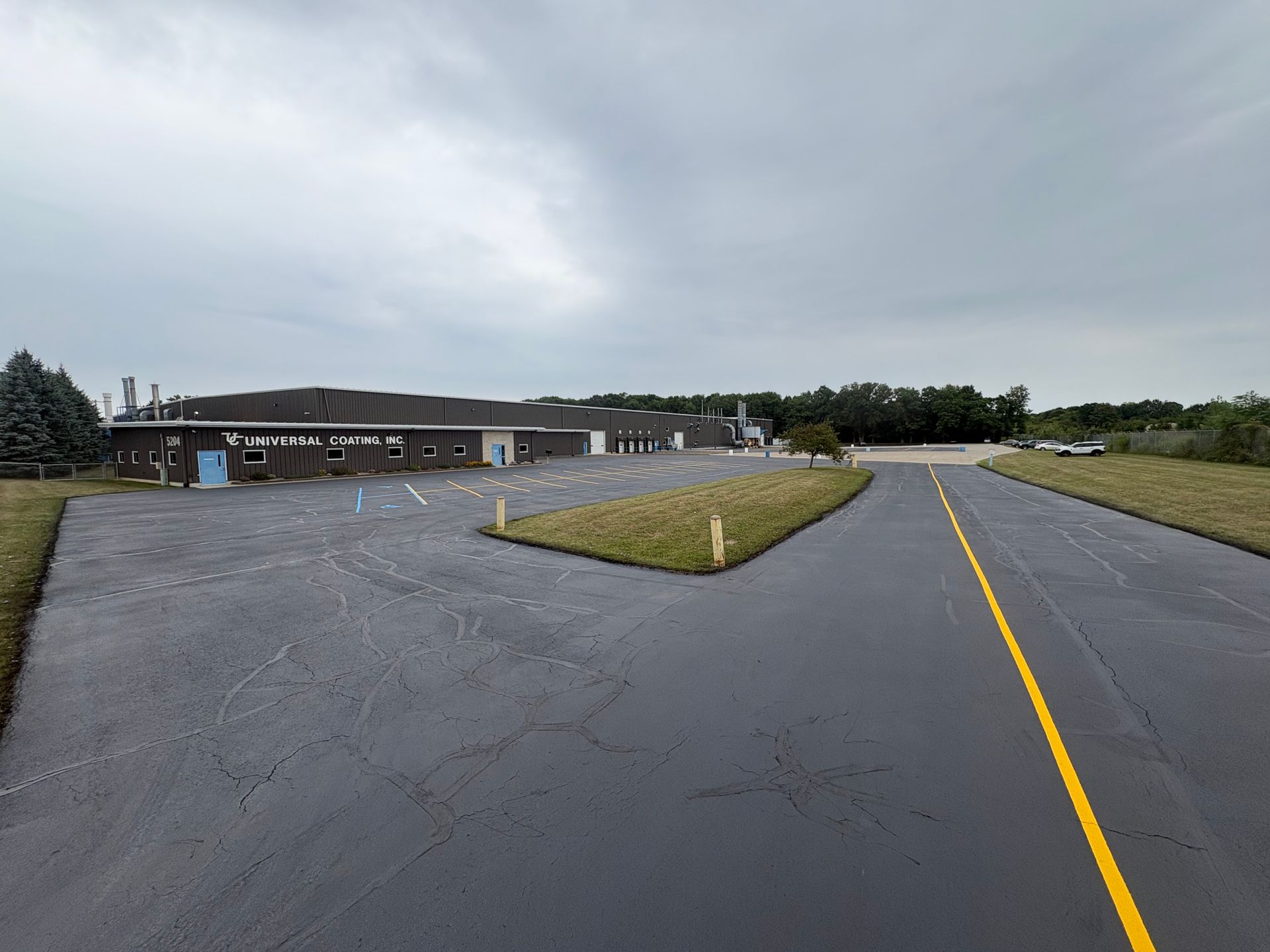Empty wet parking lot with yellow lines beside a low building under cloudy skies