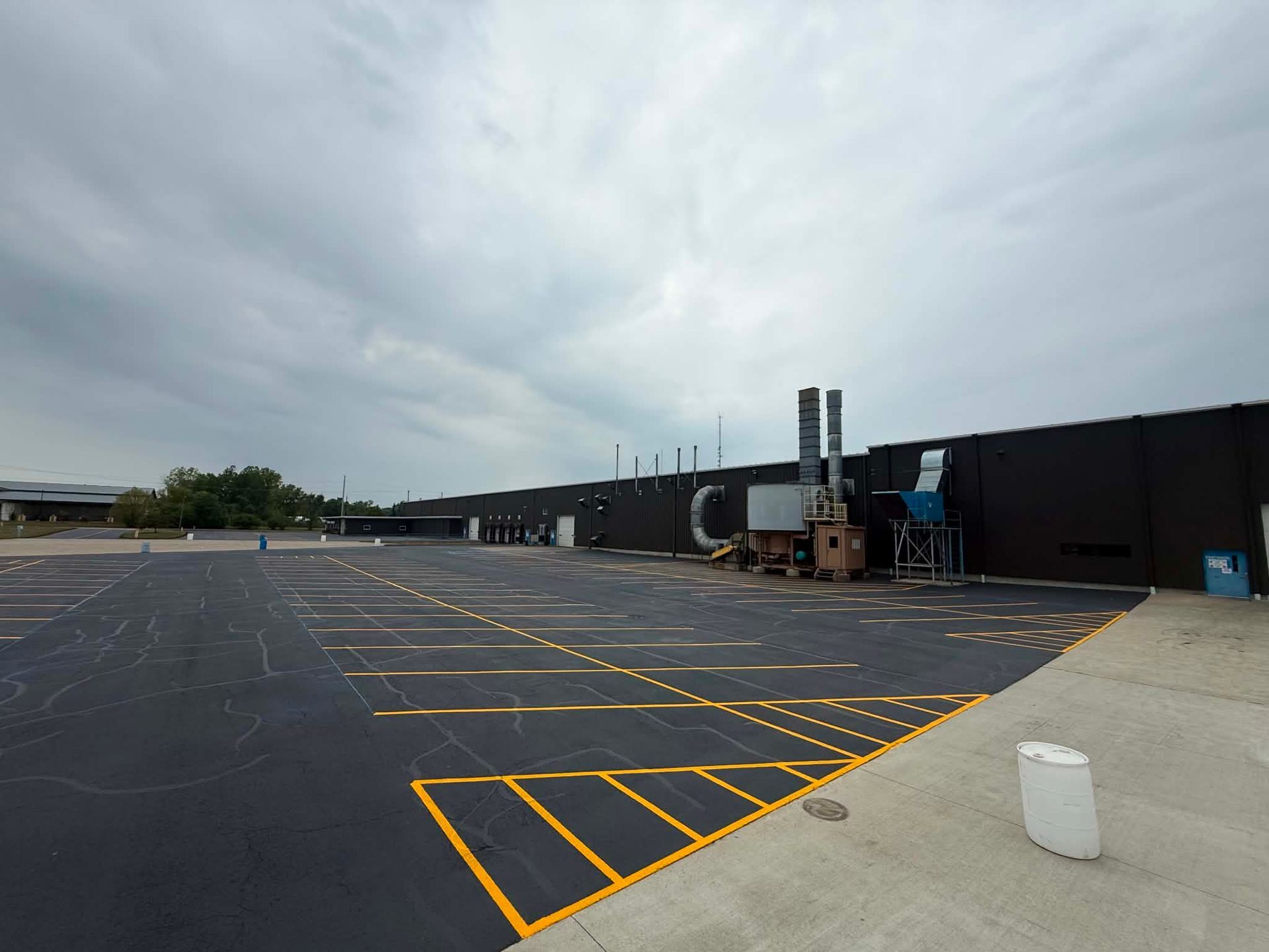 Empty parking lot with yellow lines beside a dark industrial building under an overcast sky