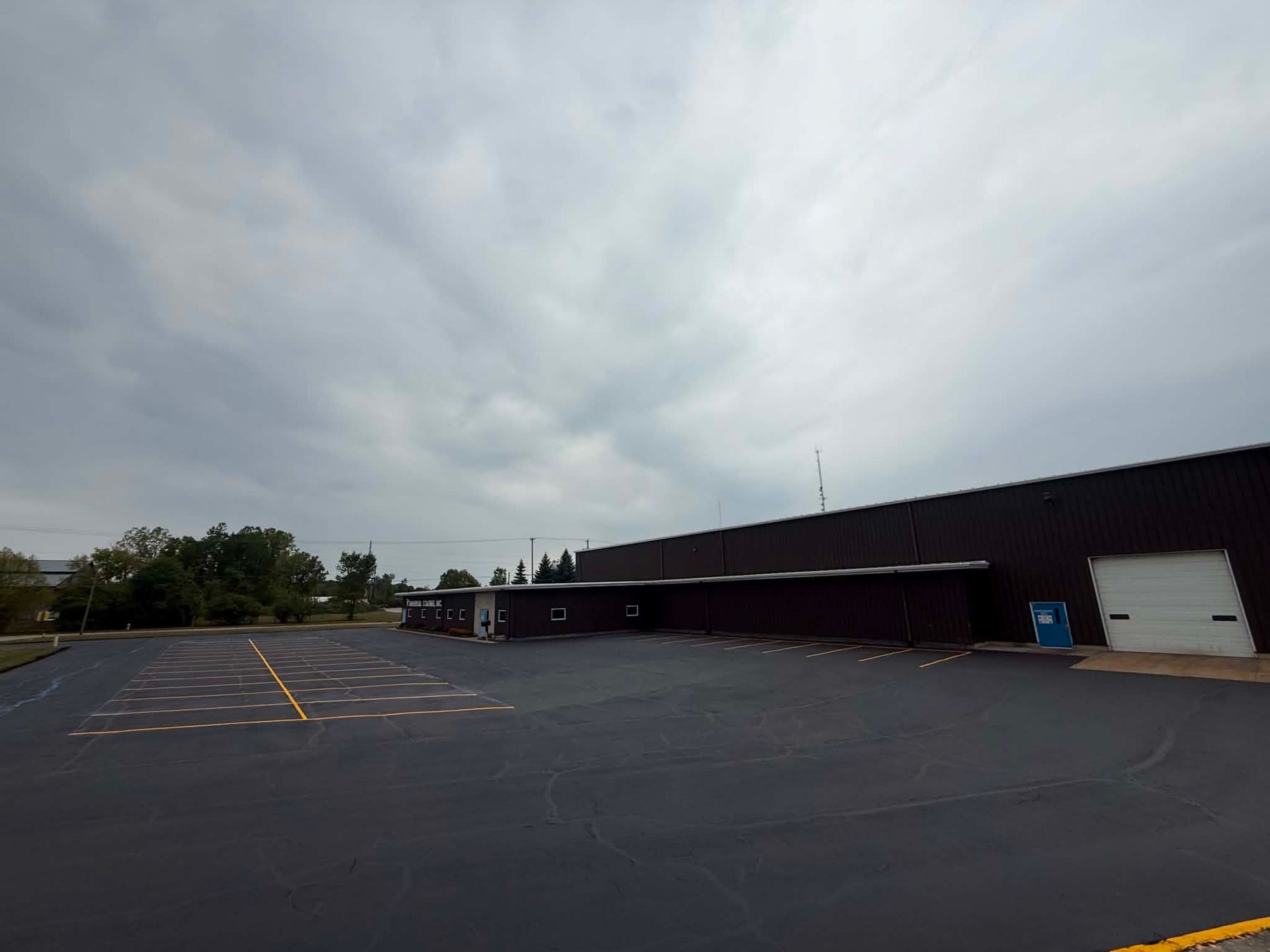 Empty parking lot beside a dark brick building under a cloudy sky.