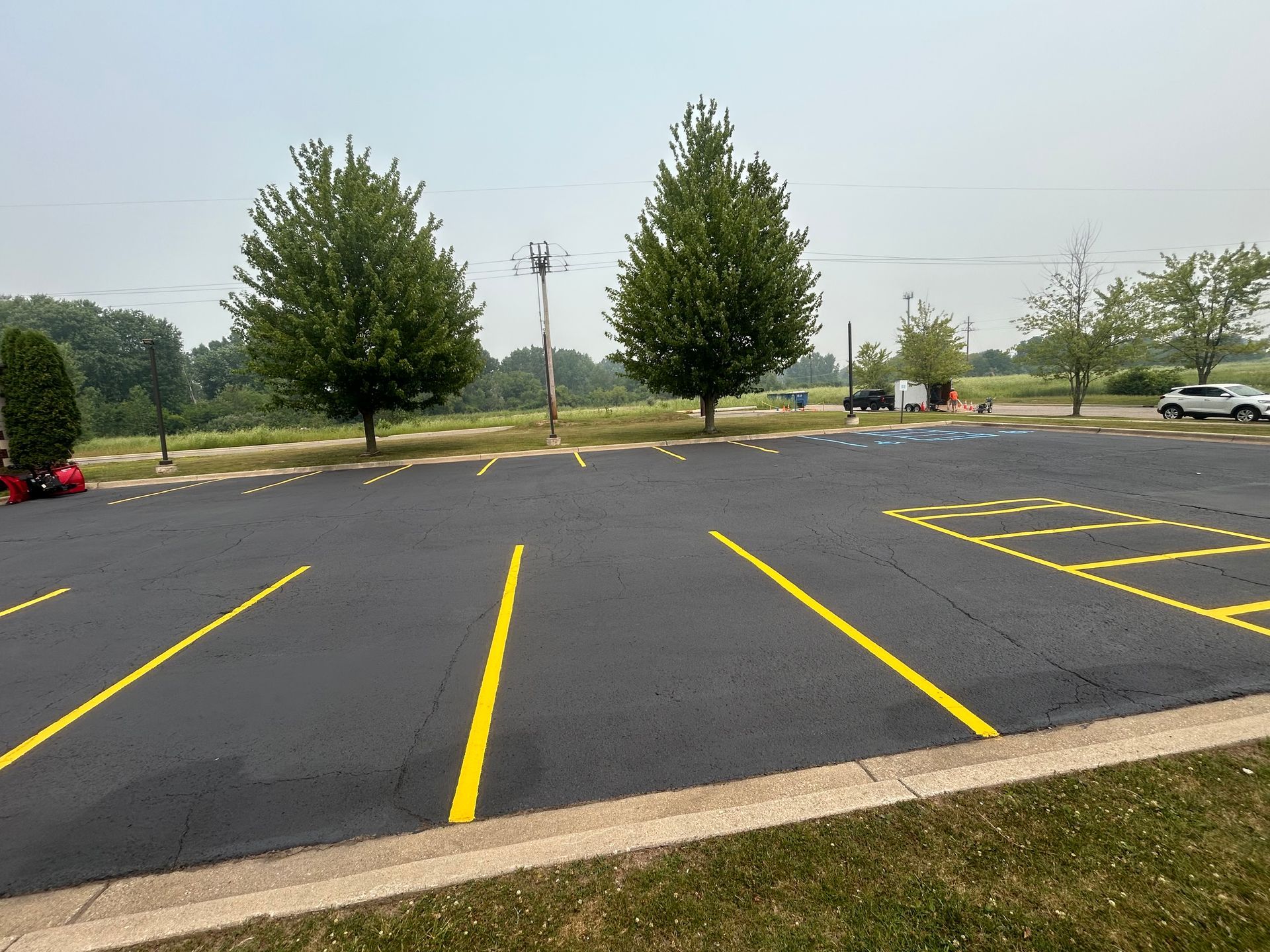 Empty parking lot with yellow painted lines, trees, and a hazy sky.