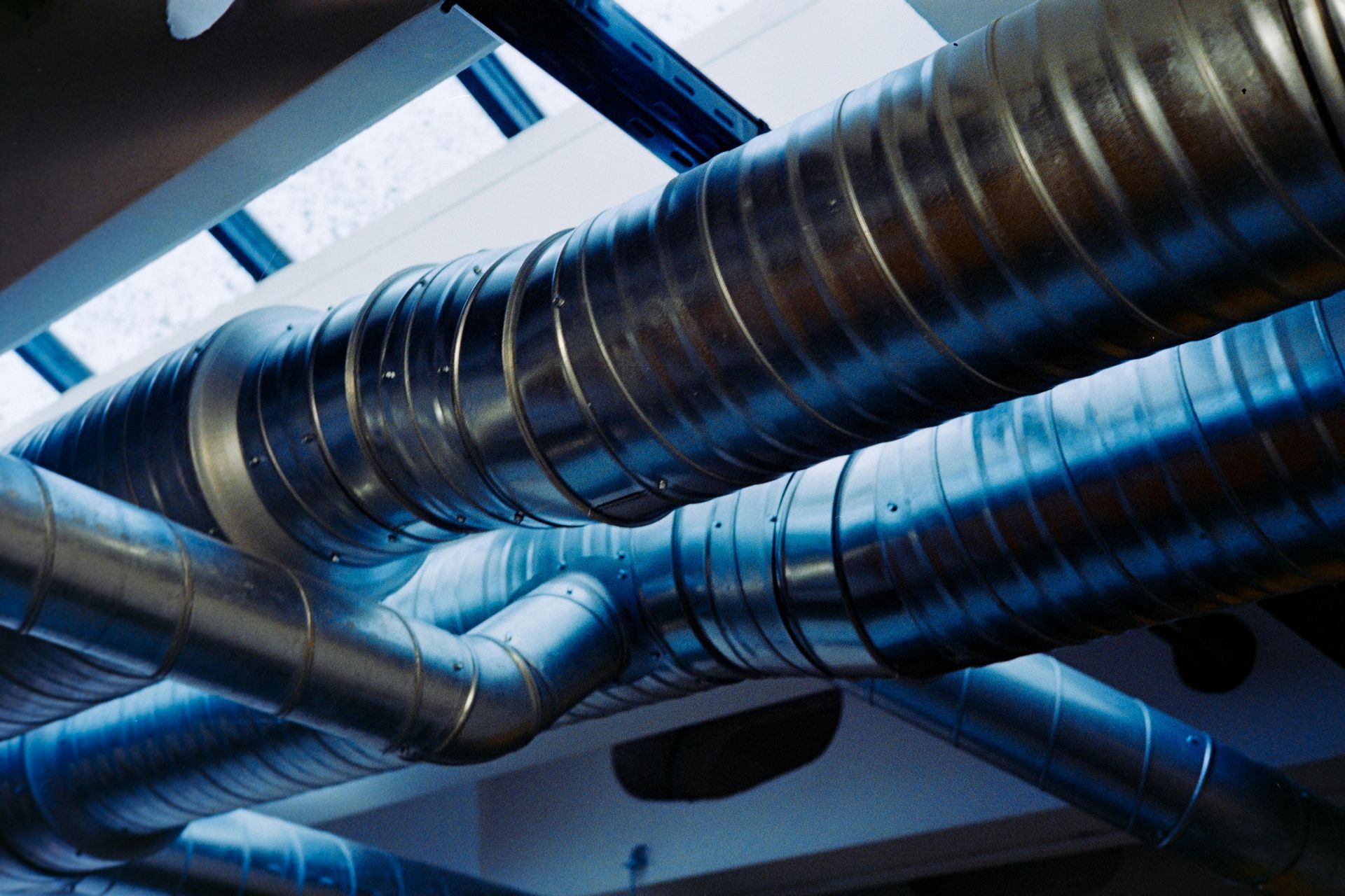 Metal ventilation ducts crisscross a blue industrial ceiling, viewed from below.