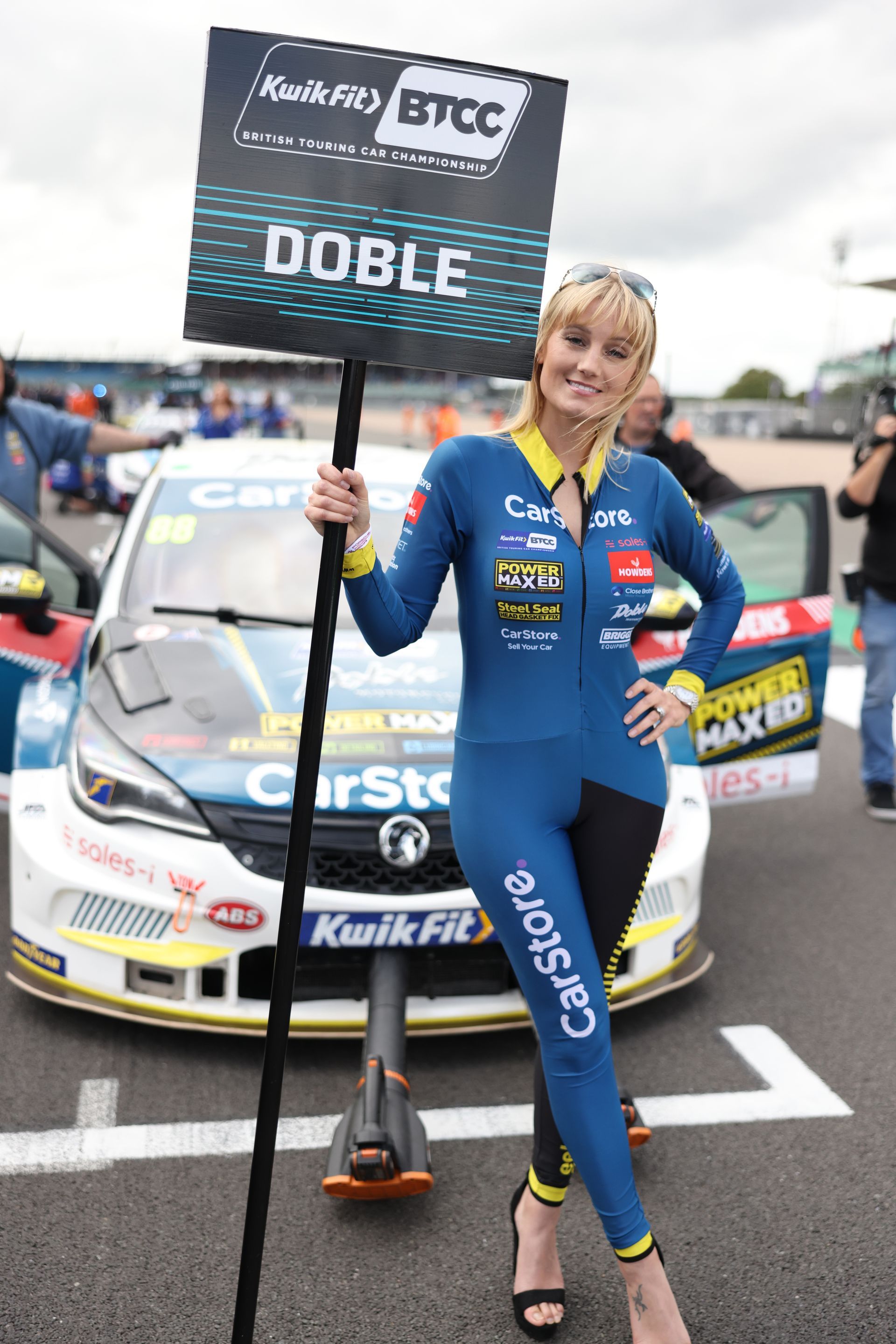 A woman is holding a sign in front of a race car.