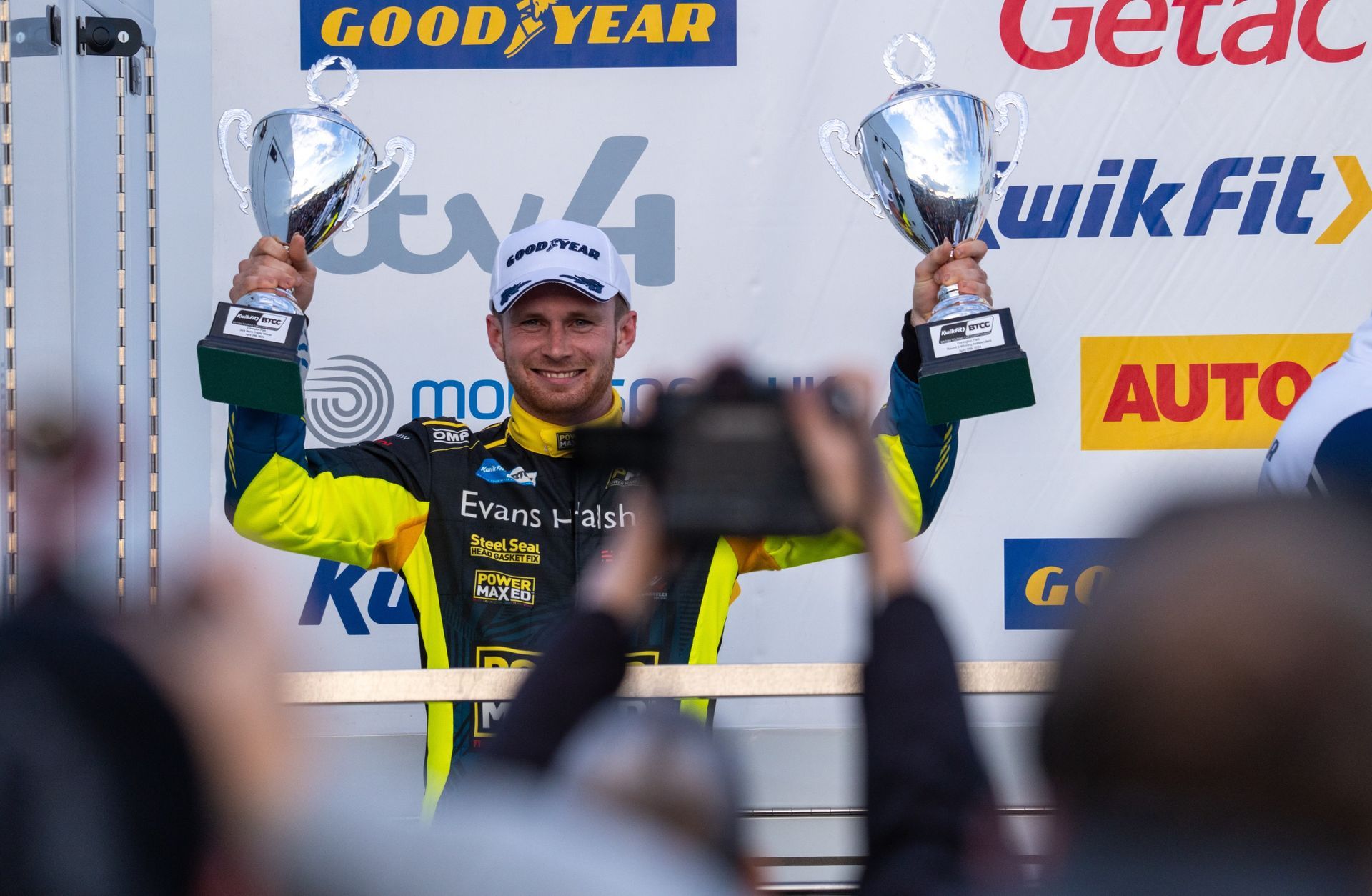 A man is holding two trophies in front of a good year sign
