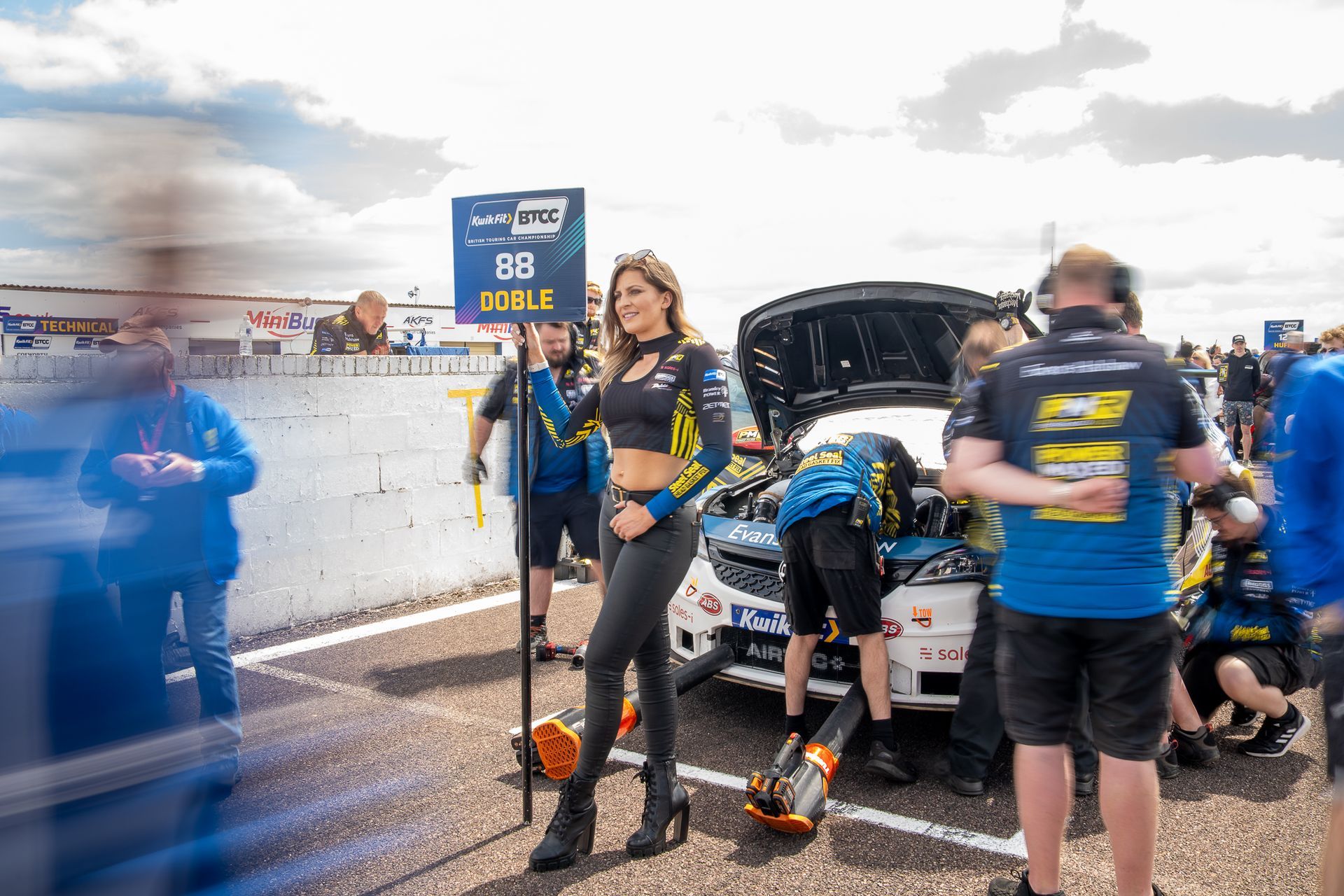A woman is standing in front of a race car at a race track.