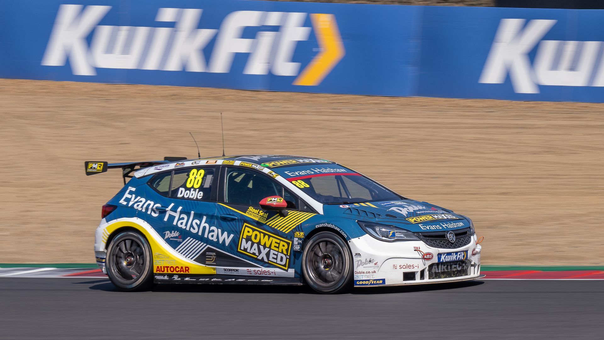 A race car is driving on a track in front of a kwikfit sign.