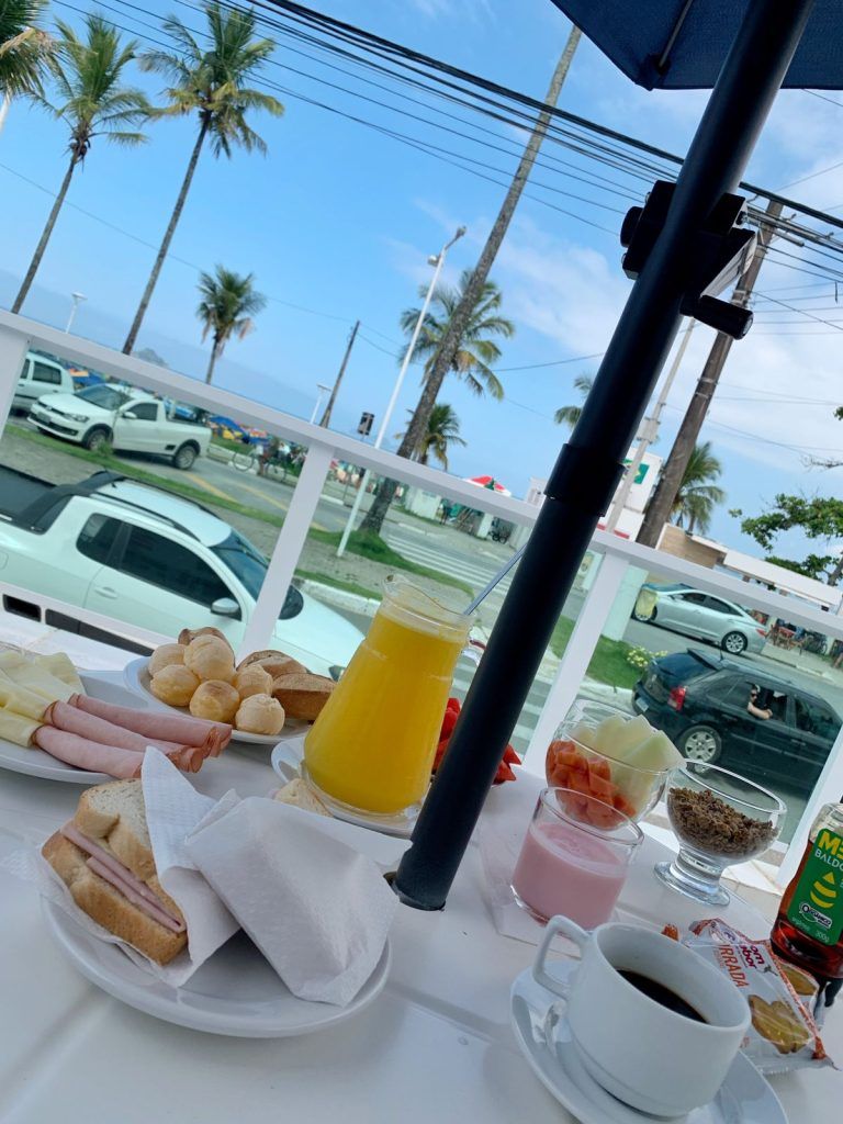Mesa de café com café, doces, suco de laranja e vista para a rua à beira-mar através da janela.