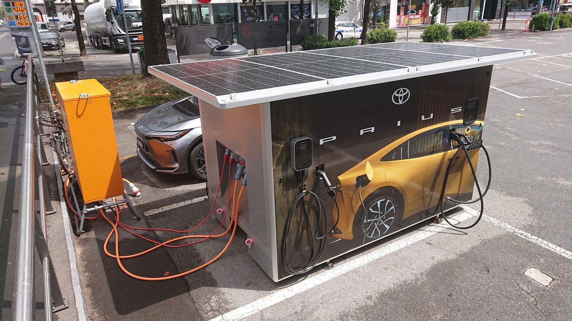 Eine solarbetriebene Ladestation mit Kabeln, die mit einem Elektroauto auf einem Parkplatz verbunden sind.