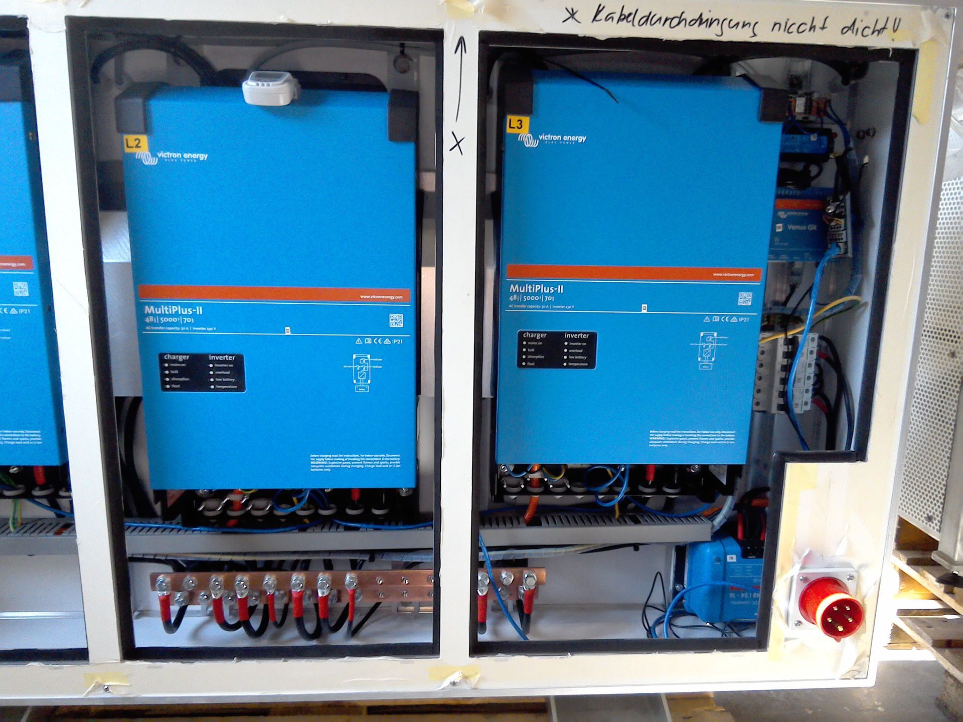 Zwei blaue Victron Energy Wechselrichter, die nebeneinander in einem Schrank montiert sind, wobei die elektrischen Leitungen und Komponenten sichtbar sind.