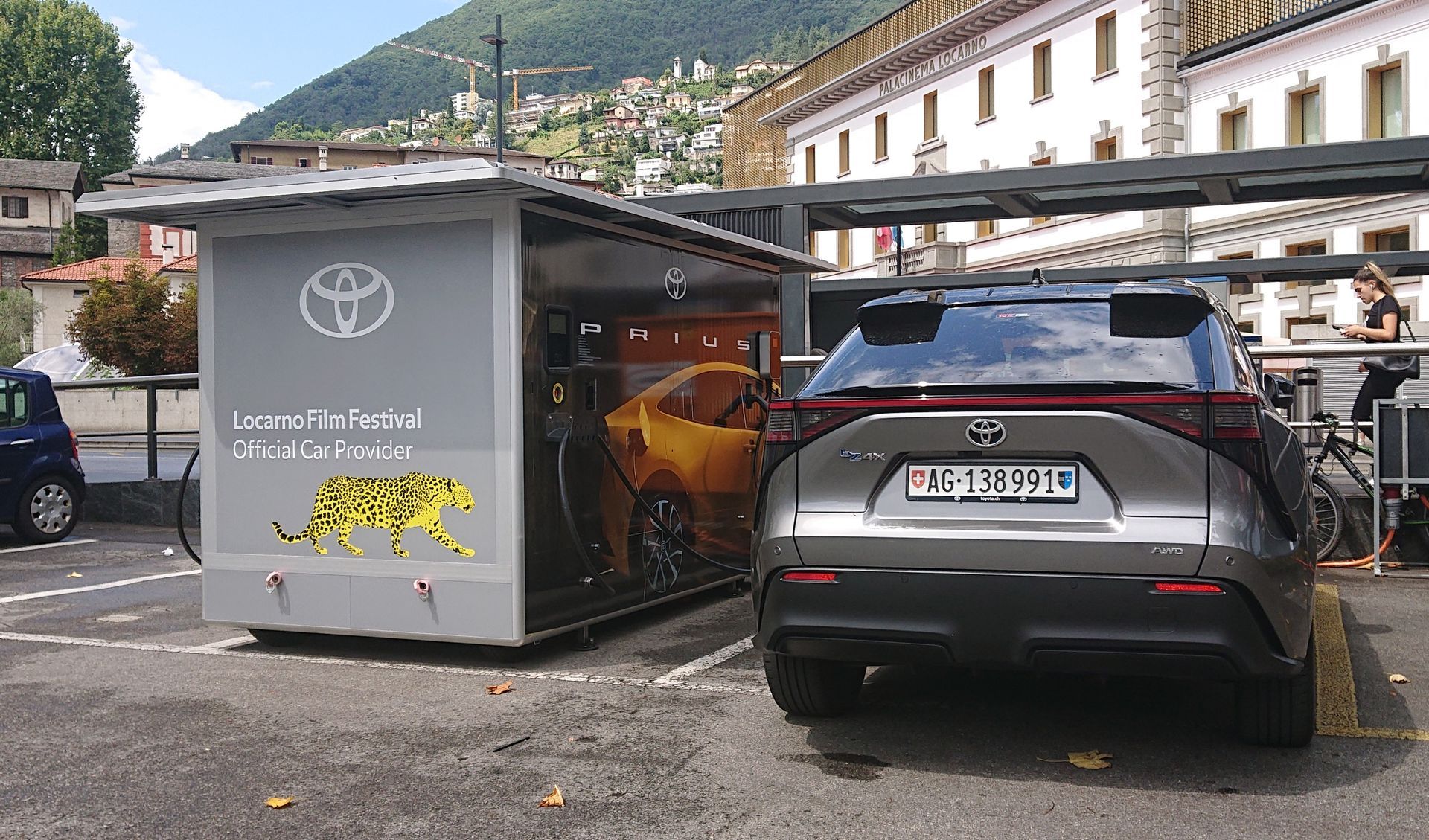 Ein grauer Toyota Mirai parkte neben einem Ladestationskiosk mit Toyota-Logo und gelber Jaguar-Grafik.