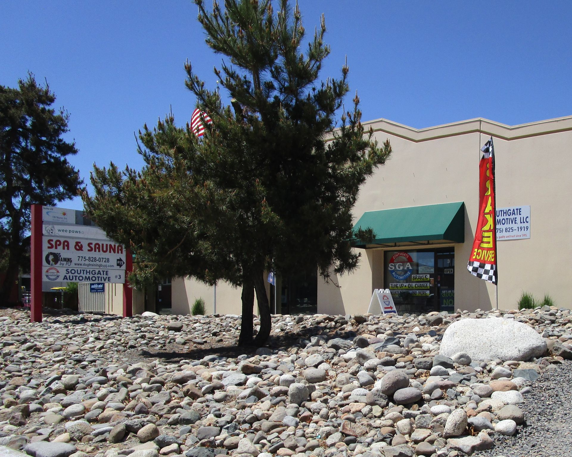 Businesses with a green awning and sign for a spa, surrounded by rocky landscaping under a blue sky. | Southgate Automotive