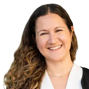 A woman with long hair is smiling and wearing a white shirt and black jacket.