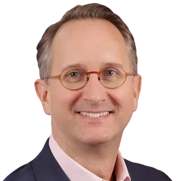 A man wearing glasses and a pink shirt is smiling for the camera.