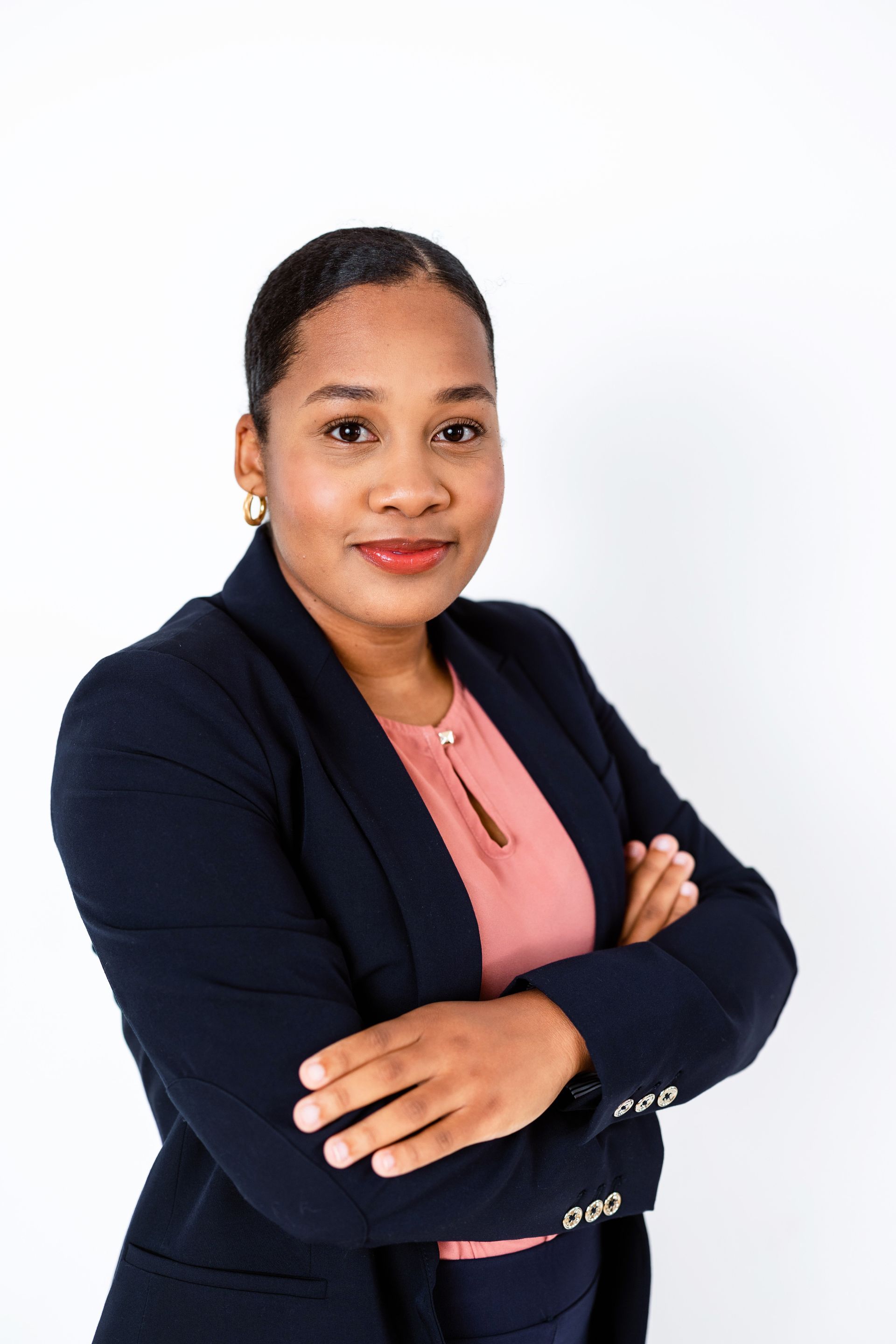 A woman in a suit and pink shirt is standing with her arms crossed.