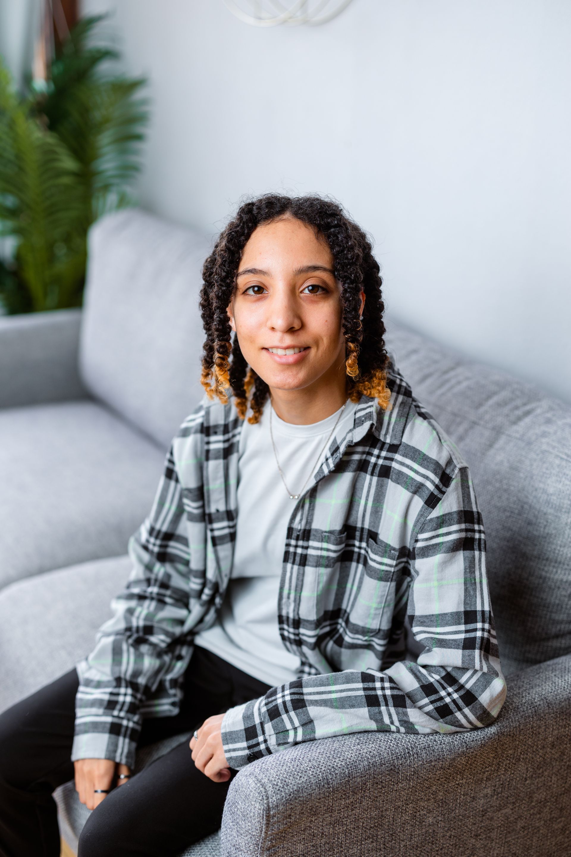 A woman is sitting on a couch wearing a plaid shirt.