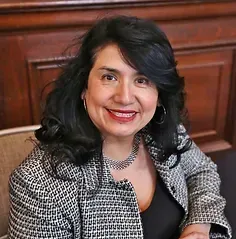 A woman wearing a black and white jacket and a necklace is smiling for the camera.