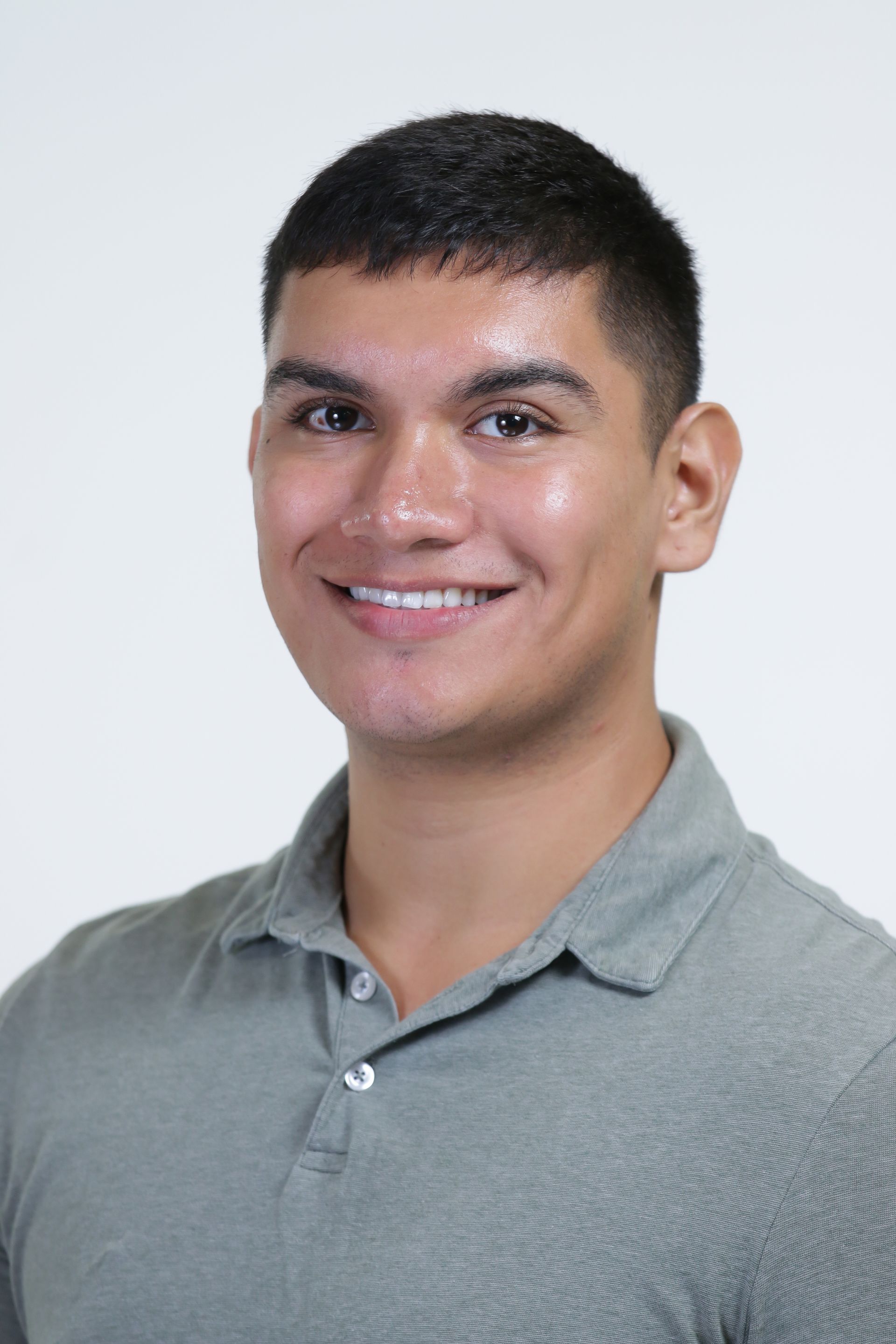 A young man in a grey polo shirt is smiling for the camera.