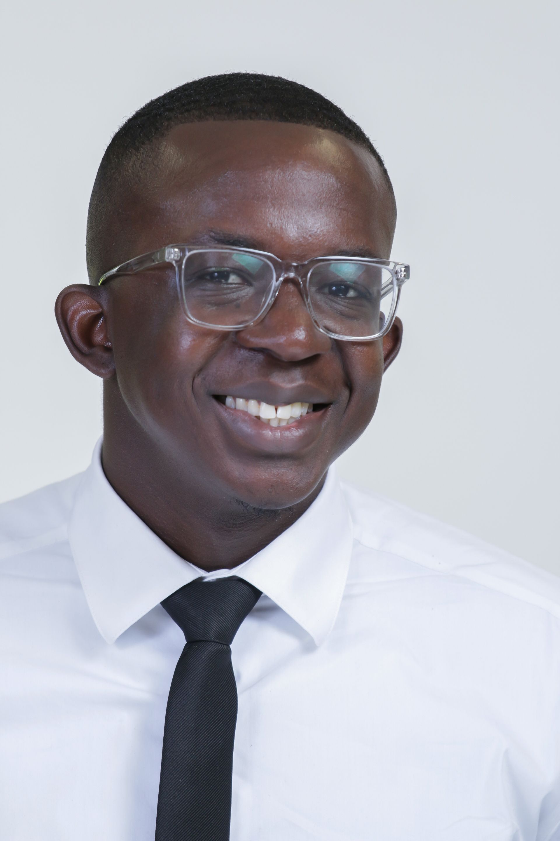 A man wearing glasses and a white shirt and tie is smiling.